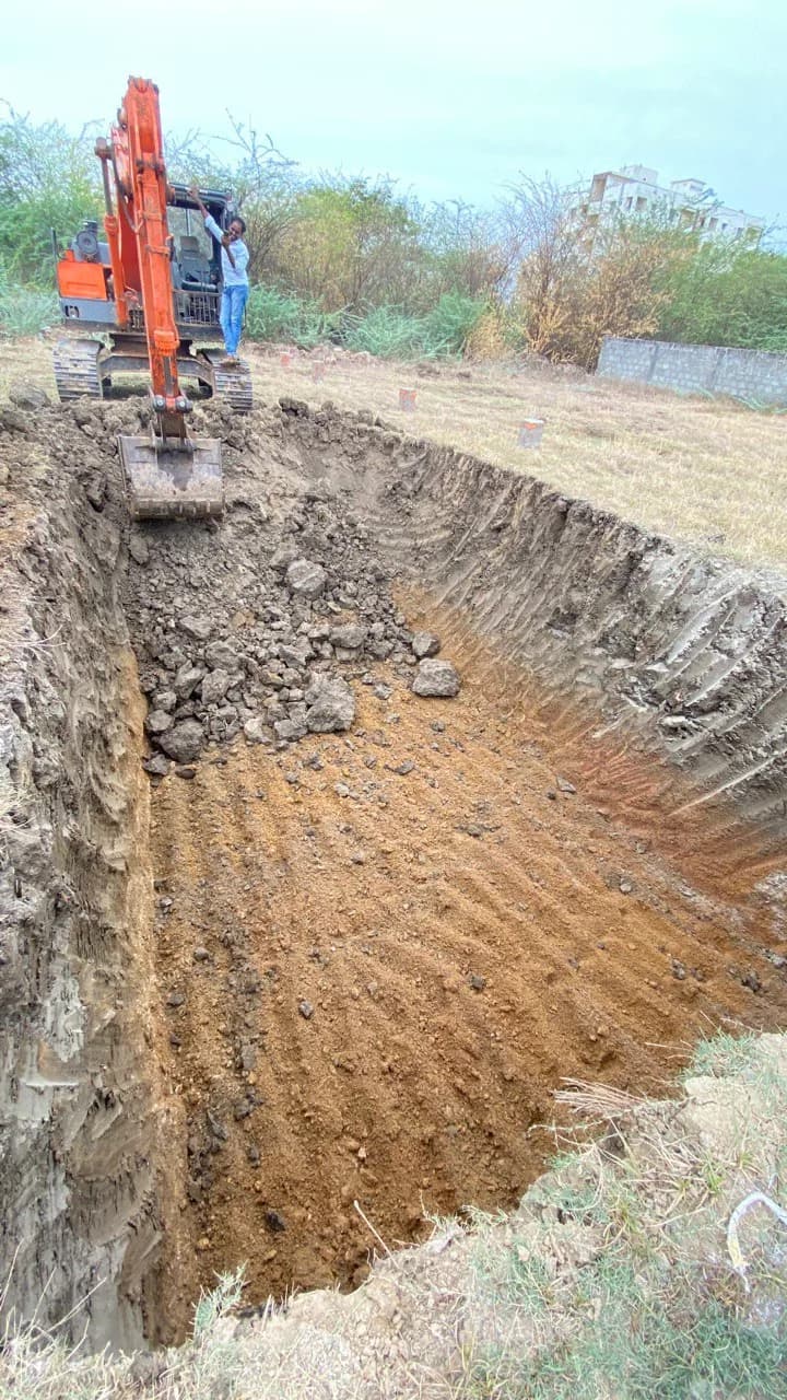 An excavator digging the foundation trenches in red earth at the church site