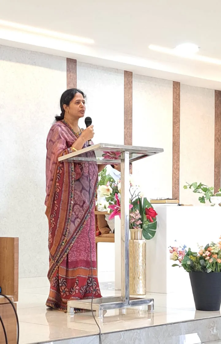 A woman in a sari speaking from the lectern during a service at Faith Temple
